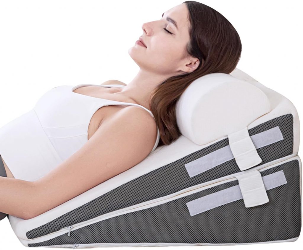 A woman reclines comfortably on an adjustable wedge pillow set, featuring a breathable mesh fabric with Velcro straps for customizable support. The set includes a soft, rounded neck pillow for added comfort. How to Sleep After a C-Section - EquipMeOT